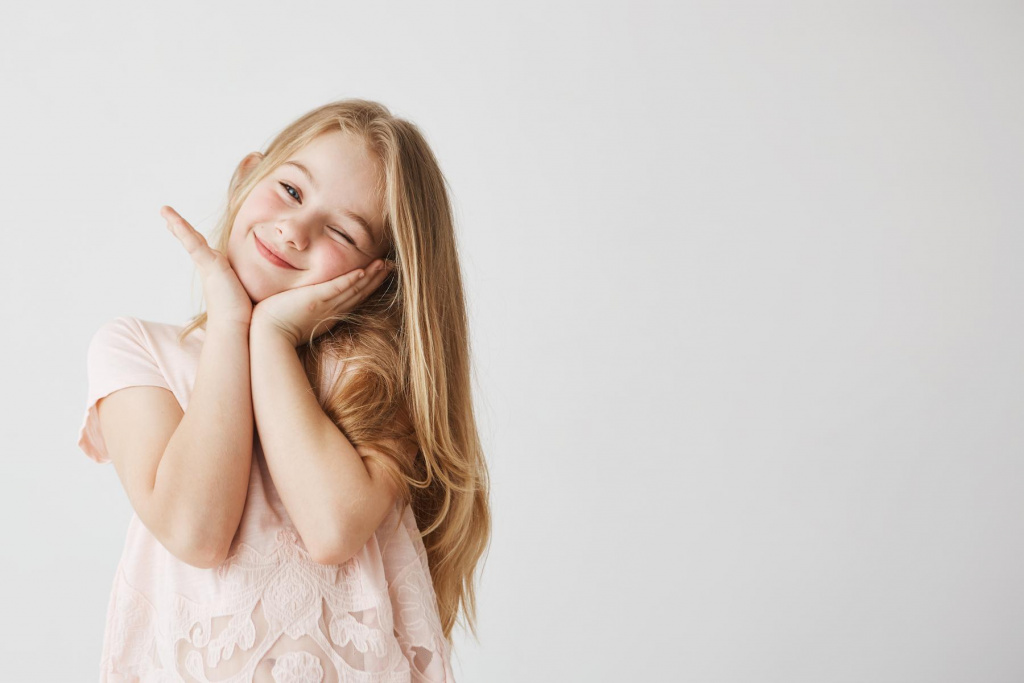 beautiful-little-blonde-girl-smiles-winking-posing-touching-face-with-her-hands-pink-cute-dress-child-looking-happy-delighted-copy-space (1).jpg